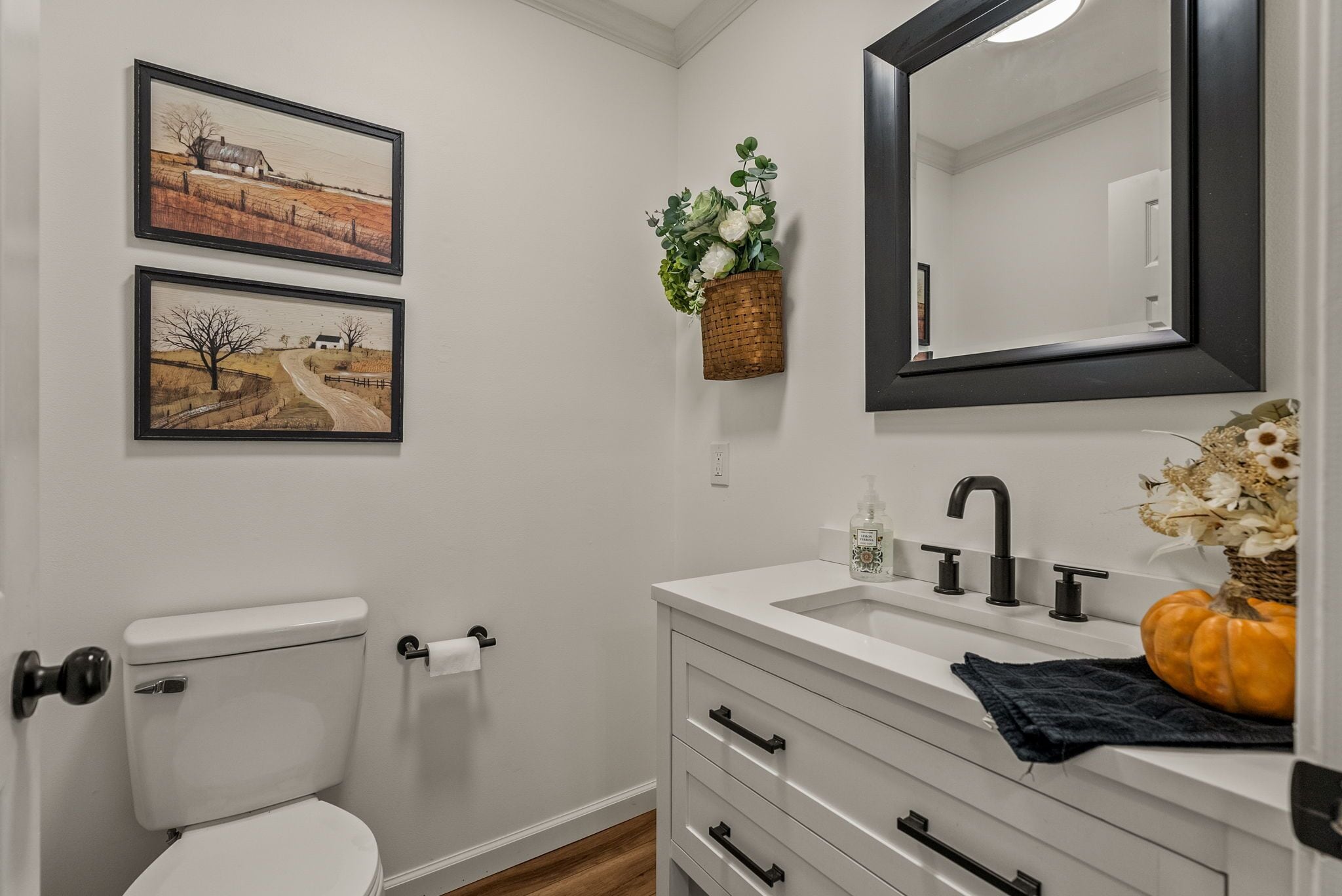 A bathroom with a toilet, sink, mirror, and two framed landscape paintings on the wall.