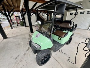 Un carrito de golf estacionado bajo una zona techada, con un garaje al fondo.
