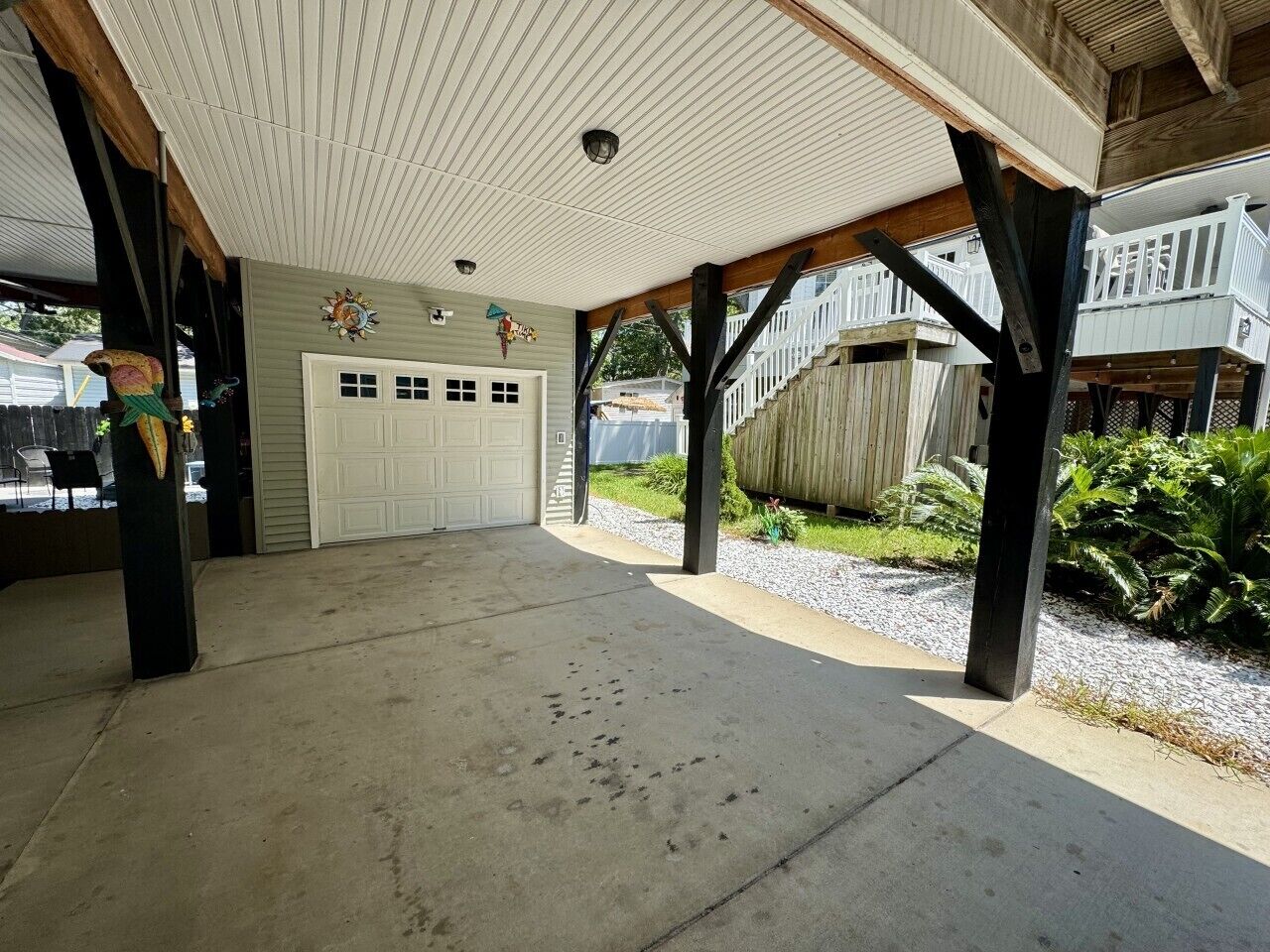 Un espace extérieur abrité doté d’un sol en béton, d’une porte de garage blanche et d’une terrasse en bois avec des garde-corps.