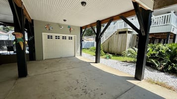 Un espace extérieur abrité doté d’un sol en béton, d’une porte de garage blanche et d’une terrasse en bois avec des garde-corps.