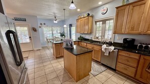 A kitchen with wooden cabinets, a black countertop island, and a refrigerator. - Ocean Lakes Beach House-Golf Cart Included-Fire Pit-King Suite-Linens (Myrtle Beach)