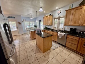 A kitchen with wooden cabinets, a black countertop island, and a refrigerator. - Ocean Lakes Beach House-Golf Cart Included-Fire Pit-King Suite-Linens (Myrtle Beach)