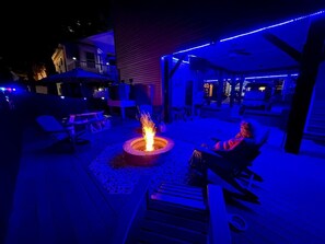 An outdoor patio area with a fire pit, seating, and ambient lighting. - The Salty Rooster | Ocean Lakes 4BR | Golf Cart + Fire Pit | Sleeps 8 (Myrtle Beach)