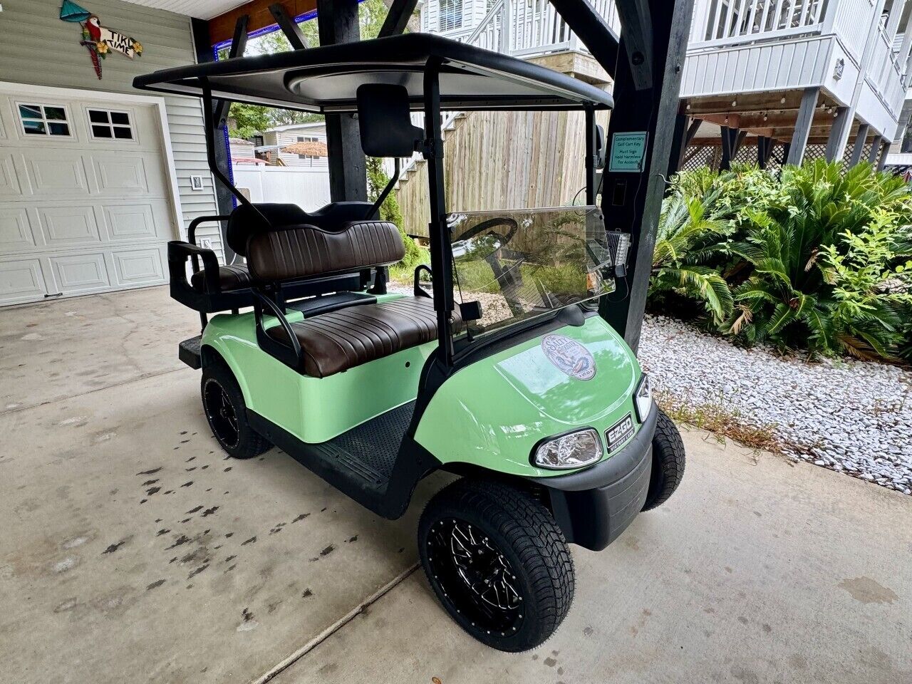 A golf cart parked in a garage with a white garage door and a wooden fence in the background.
