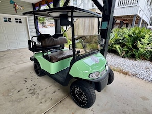Un golf cart parcheggiato in un garage con una porta bianca e una recinzione in legno sullo sfondo.