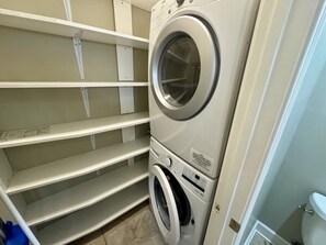 Un área de lavandería con lavadora y secadora apiladas, repisas metálicas y un inodoro blanco.