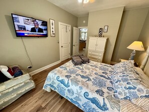 Un dormitorio con una cama, televisor, cómoda y una silla.