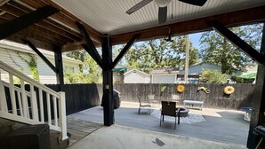 A covered patio area with a concrete floor, wooden deck, and a white railing. - Ocean Lakes Beach House-Golf Cart Included-Fire Pit-King Suite-Linens (Myrtle Beach)