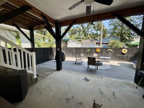 A covered patio area with a concrete floor, wooden deck, and a white railing. - Ocean Lakes Beach House-Golf Cart Included-Fire Pit-King Suite-Linens (Myrtle Beach)
