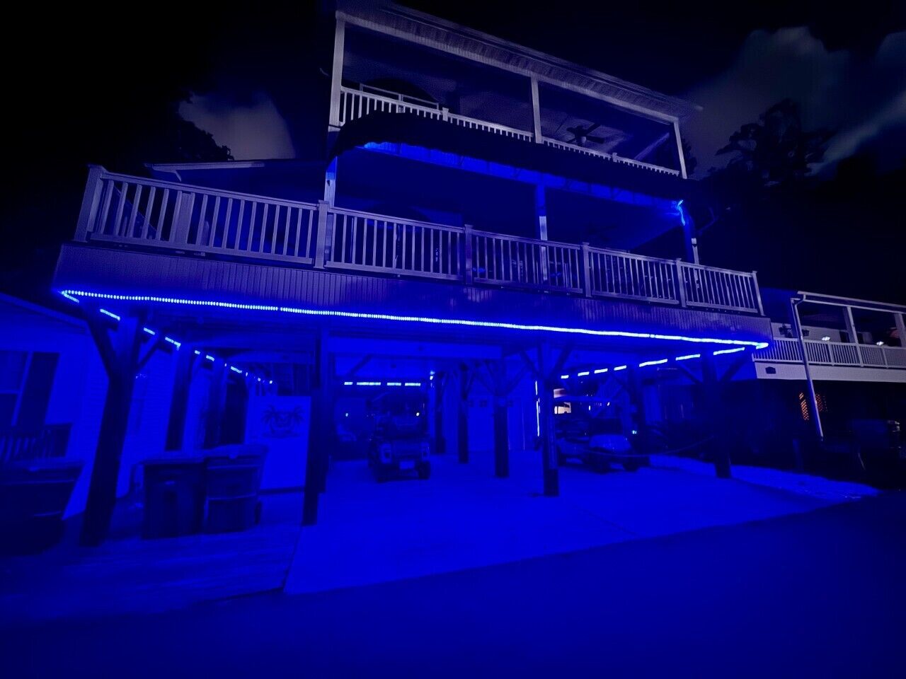 Un bâtiment à deux étages doté d’un balcon et d’un espace couvert éclairé de lumières bleues.