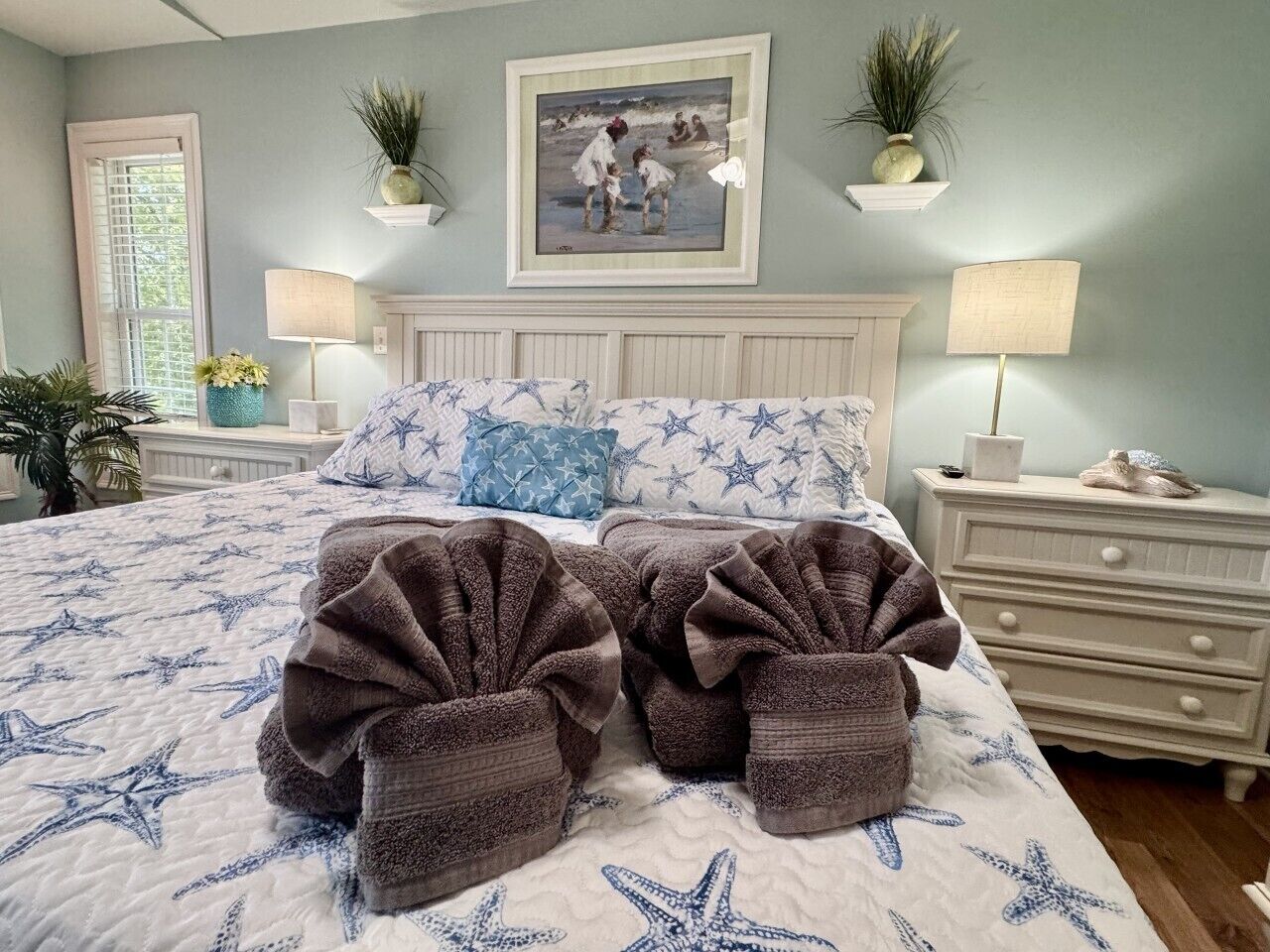 A bedroom with a bed, two bedside tables, a nightstand, a window, and a painting on the wall.