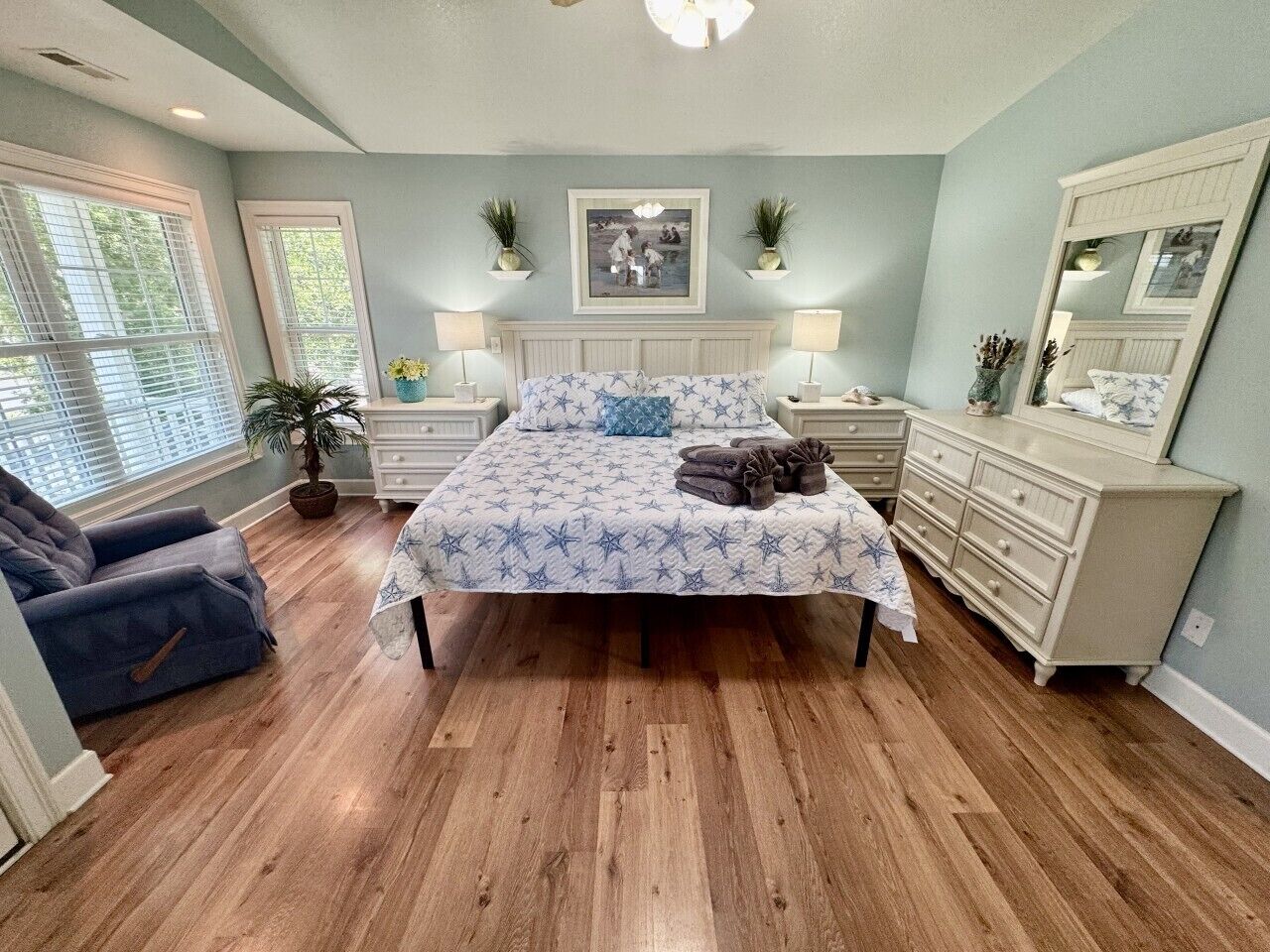 A bedroom with a bed, bedside tables, a dresser, a chair, and a large window.