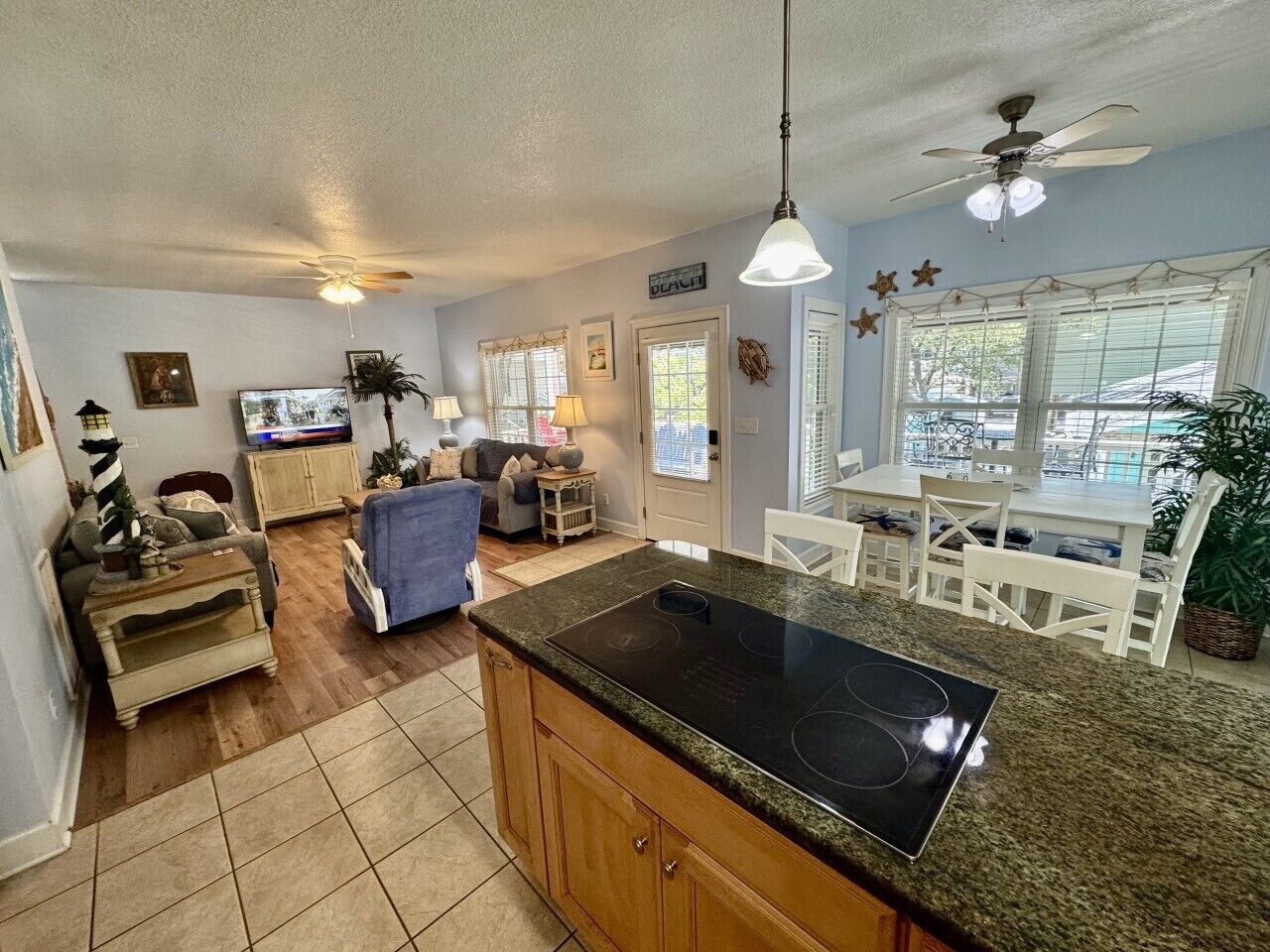 A kitchen with a central island, a dining area with white chairs, and a living room with a sofa and a television.