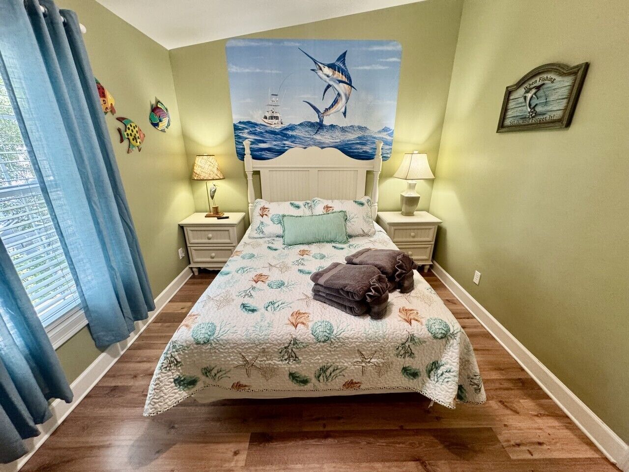 Une chambre à coucher comprenant un lit, une tête de lit, une fenêtre avec des rideaux, une table de chevet, une lampe et un élément de décoration murale.