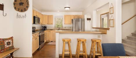 A modern kitchen with wooden cabinets, a stainless steel refrigerator, and a central island with bar stools.
