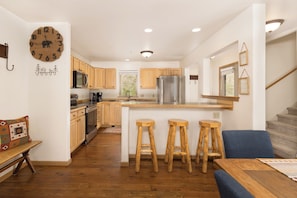 A modern kitchen with wooden cabinets, a stainless steel refrigerator, and a central island with bar stools. - The Bears Den - 4-BR chalet in Big Sky for your getaway - Private Hot Tub! (Big Sky)