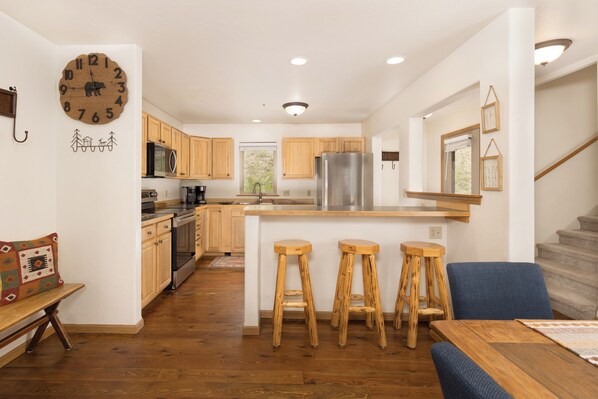 A modern kitchen with wooden cabinets, a stainless steel refrigerator, and a central island with bar stools.