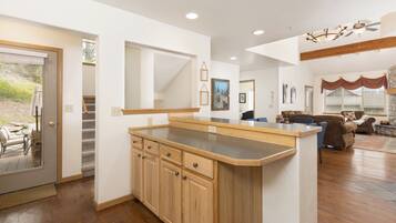 A modern kitchen with wooden cabinets and a large island, leading to a living area with a fireplace and a stone wall.