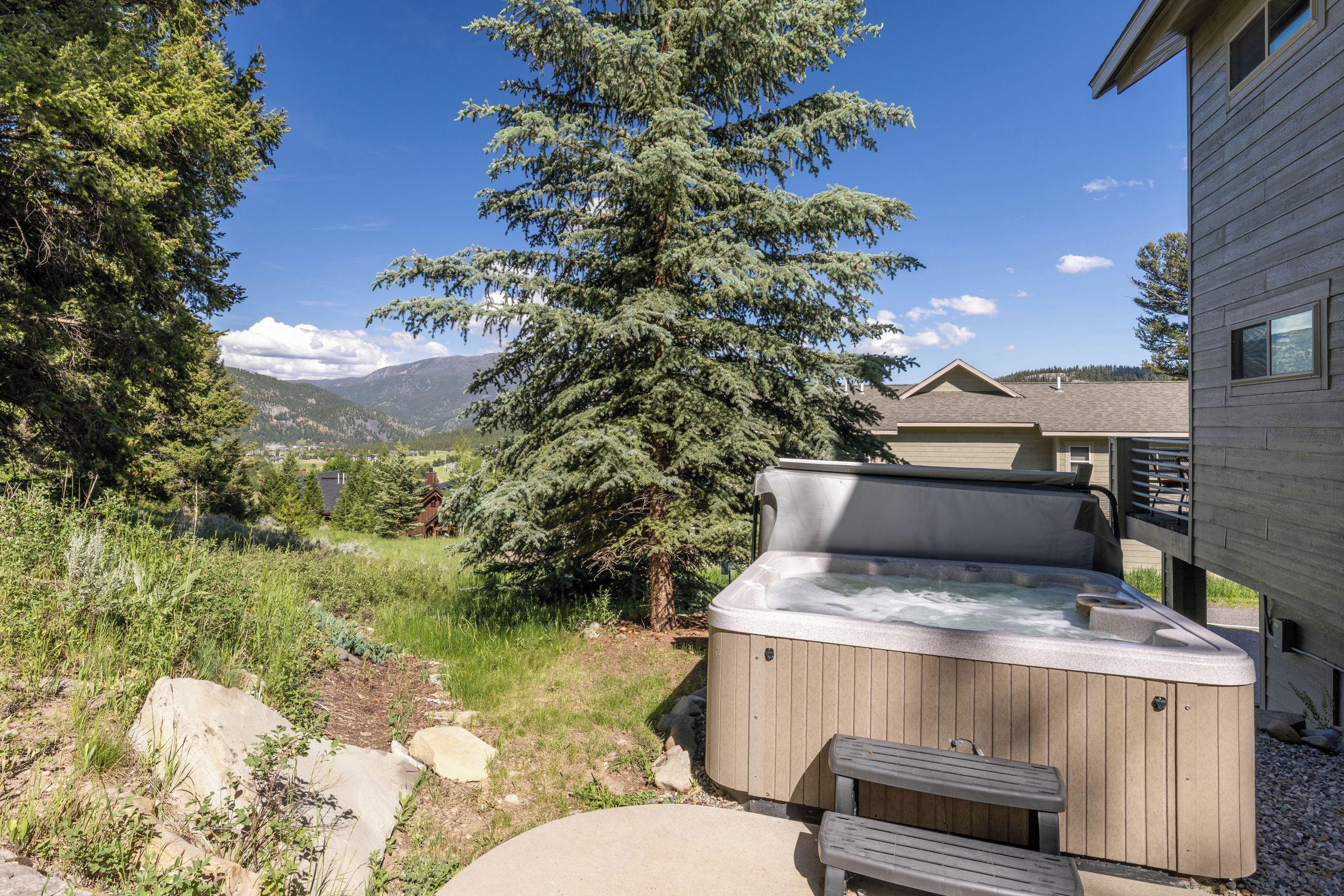 A hot tub with a wooden exterior, a bench, and a view of a mountain range in the background.