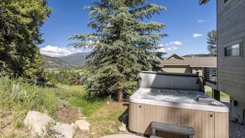 A hot tub with a wooden exterior, a bench, and a view of a mountain range in the background.
