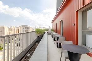 A balcony with a city view, outdoor seating, and a red building facade. - VN Turiassu (São Paulo)