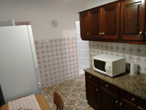 A kitchen with a microwave, cabinets, a refrigerator, and patterned tiles.
