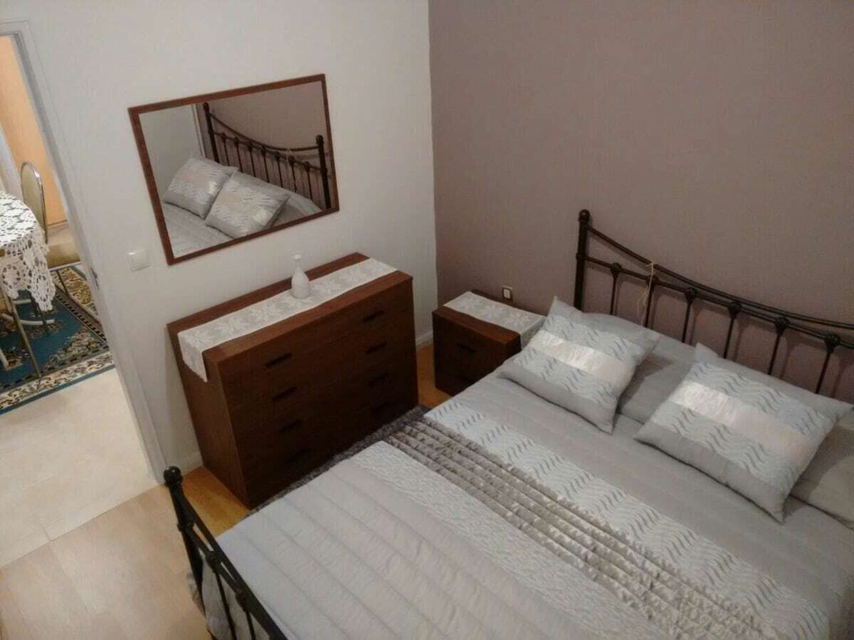 A bedroom with a bed, a dresser, a nightstand, a mirror, and a window.