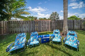 A backyard with a wooden fence, a palm tree, and four lawn chairs with a floral pattern. - 2600 Managed by Brampton Park (Pompano Beach)