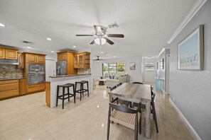 A modern kitchen with built-in appliances, a dining area with a wooden table and chairs, and a ceiling fan. - 2600 Managed by Brampton Park (Pompano Beach)