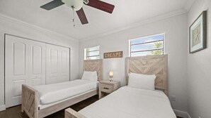 A bedroom with two single beds, a nightstand with a lamp, a ceiling fan, and a window with blinds. - 2600 Managed by Brampton Park (Pompano Beach)