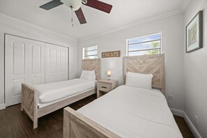 A bedroom with two single beds, a nightstand with a lamp, a ceiling fan, and a window with blinds. - 2600 Managed by Brampton Park (Pompano Beach)