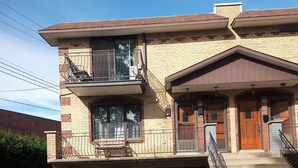 A two-story building with a garage, a balcony, and a staircase leading to the entrance. - Cozy 2 bedroom close to downtown, public transportation & airport (Montréal)