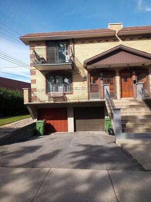 A two-story building with a garage, a balcony, and a staircase leading to the entrance. - Cozy 2 bedroom close to downtown, public transportation & airport (Montréal)