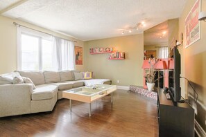 A living room with a sectional sofa, a glass coffee table, a flat-screen TV, and a bookshelf. - Cozy 2 bedroom close to downtown, public transportation & airport (Montréal)