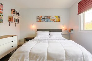 A bedroom with a large bed, bedside tables, a dresser, a wall-mounted shelf with books, and a painting. - Cozy 2 bedroom close to downtown, public transportation & airport (Montréal)