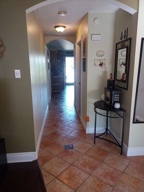 A hallway with a tiled floor, a black table with a white cup, and a mirror on the wall. - Cozy 2 bedroom close to downtown, public transportation & airport (Montréal)
