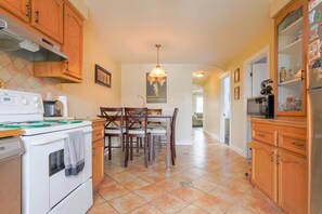 A kitchen with wooden cabinets, a dining table with chairs, a hanging light fixture, and a refrigerator. - Cozy 2 bedroom close to downtown, public transportation & airport (Montréal)
