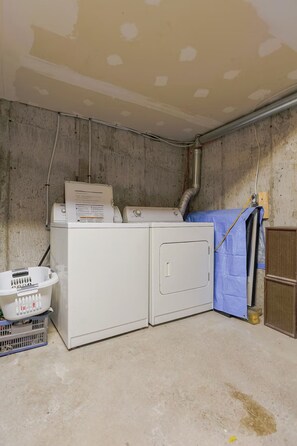 A laundry area with a washing machine, dryer, and a utility room with exposed pipes and unfinished walls. - Cozy 2 bedroom close to downtown, public transportation & airport (Montréal)