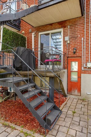 A brick building with a metal staircase leading to a covered outdoor area. - Cozy 2 bedroom close to downtown, public transportation & airport (Montréal)