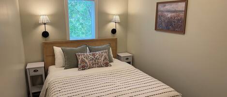 A bedroom with a bed, two bedside lamps, a window, and a wall-mounted picture.