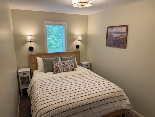 A bedroom with a bed, two bedside lamps, a window, and a wall-mounted picture.