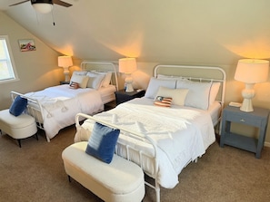 A hotel room with two beds, each with a nightstand and lamp, a small chair, and a radiator.