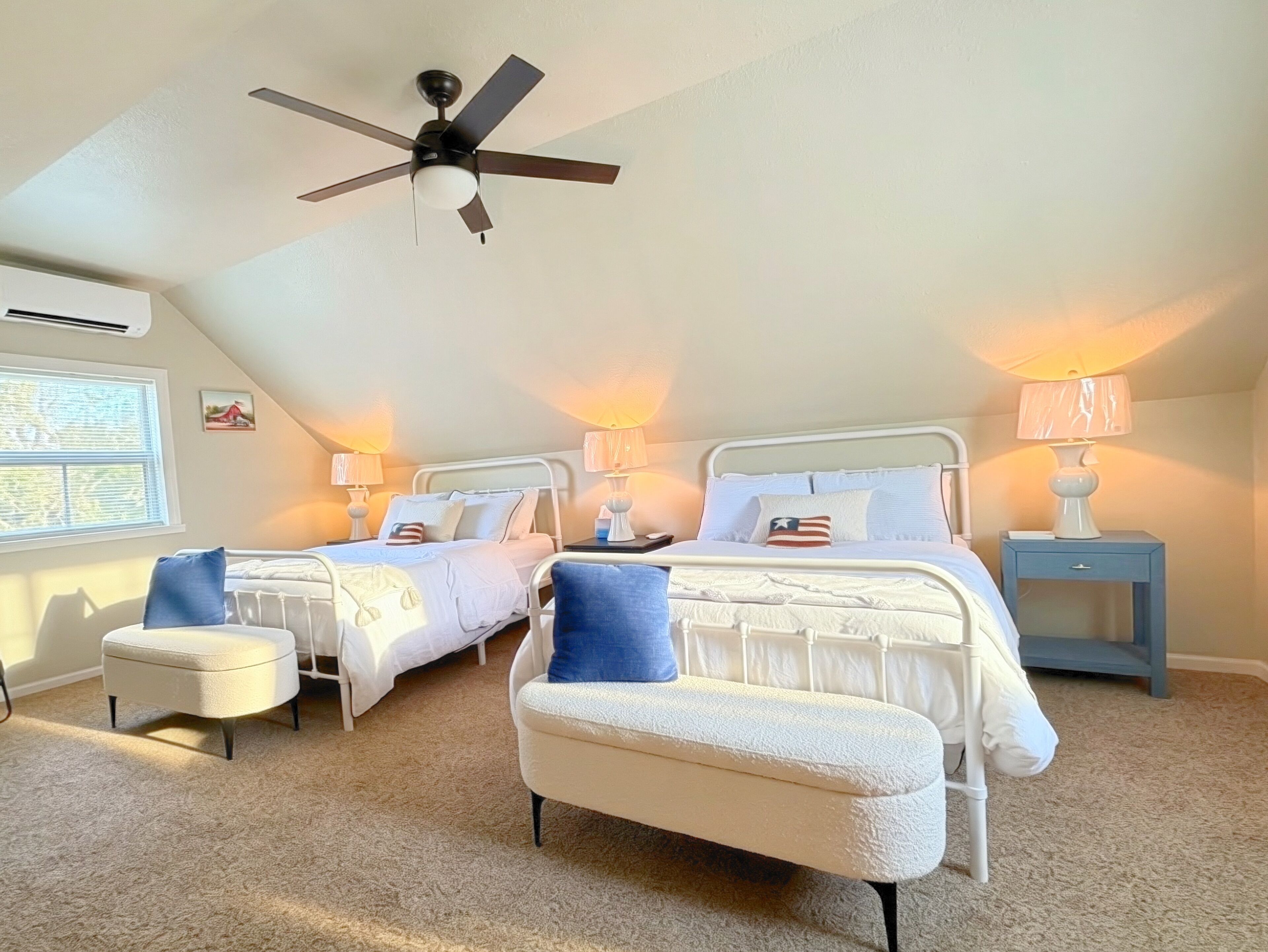 A bedroom with two beds, a ceiling fan, bedside lamps, a window, and a carpeted floor.