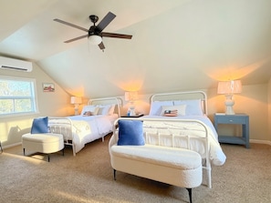 A bedroom with two beds, a ceiling fan, bedside lamps, a window, and a carpeted floor.