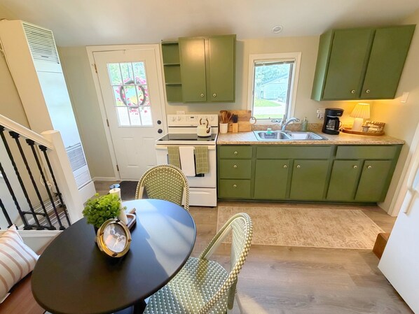 A kitchen with green cabinets, a stove, a sink, and a dining area with a table and chairs.