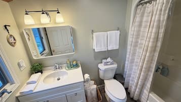 Un baño con lavamanos, espejo, inodoro y cortina de ducha.