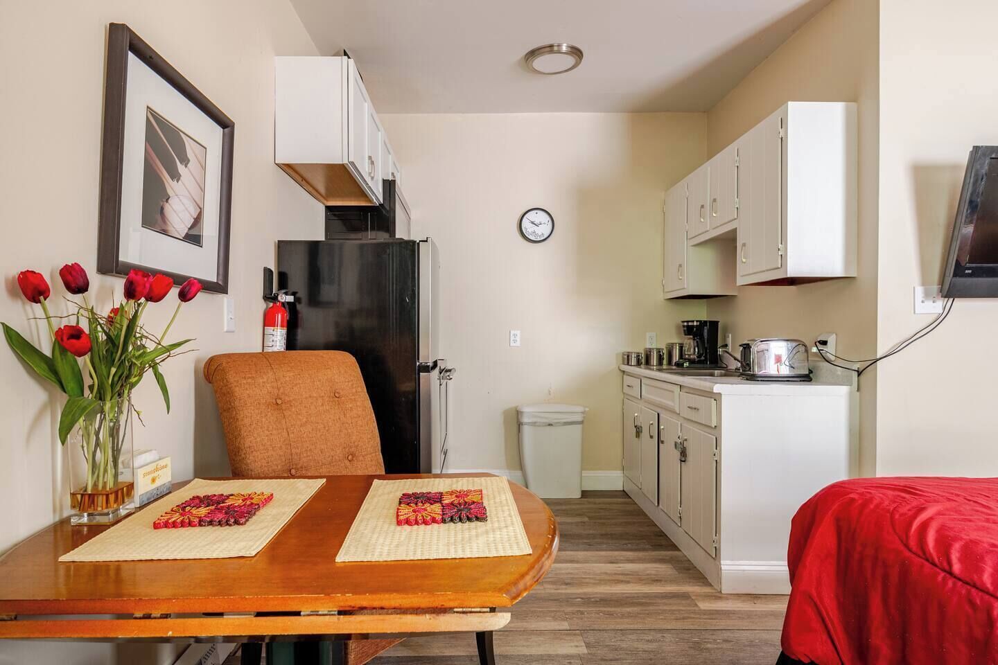 A compact kitchen with white cabinets, a black refrigerator, and a clock on the wall.