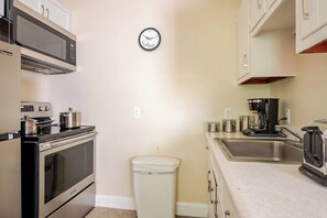 Cocina compacta con estufa, microondas, fregadero y un reloj en la pared.
