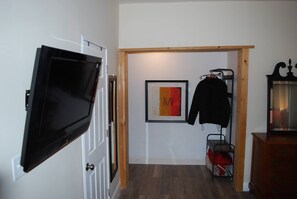 Un pasillo con un televisor montado en la pared, una obra de arte enmarcada, un perchero con una chaqueta y un mueble de madera.