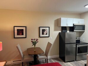A compact kitchen with a dining table, chairs, a refrigerator, a microwave, and a stove.